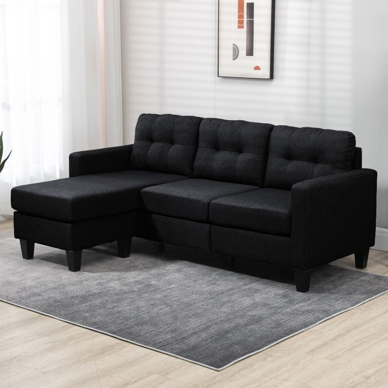 Black sectional sofa in a living room setting with a gray rug and white walls.
